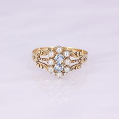 What a remarkable ring! This antique 9-10K gold carved ring features 8 seed pearls and 2 modern replacement round aquamarines. It is lightweight, so not recommended for daily wear. Save her for special occasions to elevate your look!   This antique ring is in good wearable condition, it does show some normal wear, and old marks inside the ring of a trefoil and a W. It comes in a size 8, but it can be sized up or down for you!