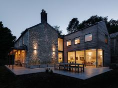 a house that is lit up at night with lights on the windows and outside furniture