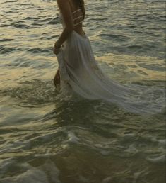 a woman standing in the water wearing a white dress