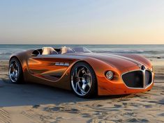 an orange sports car is parked on the sand near the water and beach at sunset