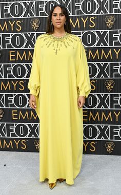 a woman standing in front of a wall wearing a long yellow dress with beaded neckline