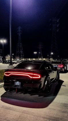 the rear end of a black sports car parked in a parking lot at night with its lights on