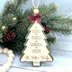 a wooden christmas tree ornament hanging from a pine tree with a red ribbon