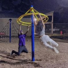 two young men playing with a yellow and blue hoop on a playground at night time