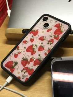 a phone case with strawberries on it sitting next to an apple laptop and headphones