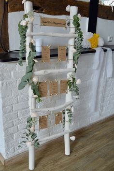 a white ladder decorated with greenery and seating cards for guests to sign on it