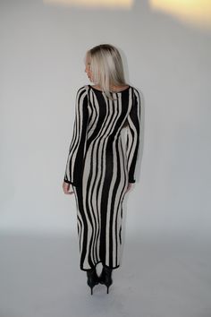 a woman standing in front of a white wall wearing a black and white striped dress