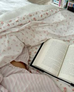 an open book laying on top of a bed next to a person in pink pajamas