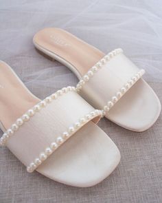 a pair of white shoes with pearls on the bottom and straps, sitting on top of a bed