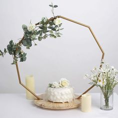 a cake with flowers and greenery on a plate next to two candles, one is white