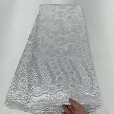 a hand is holding the edge of a piece of silver lace on a white surface