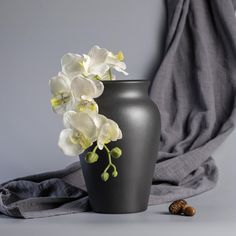 a black vase with white flowers in it next to a gray blanket and nuts on the ground