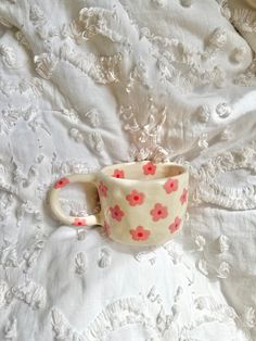 a cup sitting on top of a bed covered in white lace and red flowered fabric