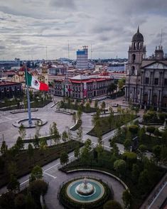 an aerial view of a city square with a fountain and flags flying in the wind