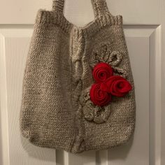 a handbag hanging on a door handle with red felt roses attached to the handles