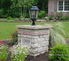 a lamp post in front of a house with flowers and plants around it on the lawn