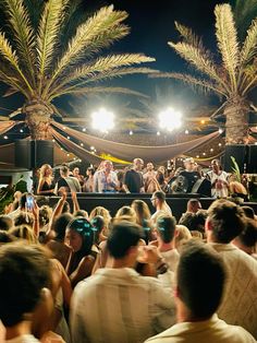 a group of people standing in front of a stage with palm trees and lights on it