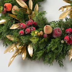 a christmas wreath with berries, pine cones and gold leaves on a white wall background