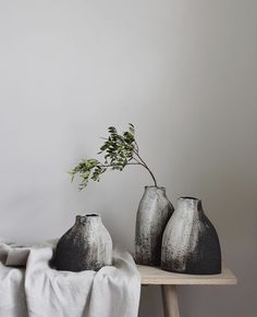 three black and white vases sitting on a wooden table next to a plant in a vase