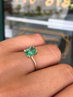 a woman's hand holding a ring with an emerald colored stone in the middle