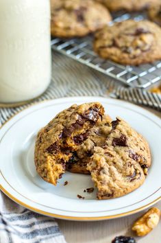 two chocolate chip cookies on a white plate with a glass of milk in the background