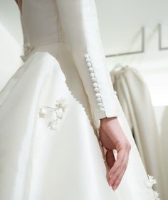 a woman in a white wedding dress holding her hand on the back of her dress