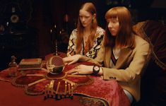 two young women sitting at a table looking at an object on it's surface