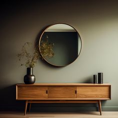 a round mirror on the wall above a wooden dresser with vases and plants in it