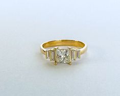 a yellow gold ring with three baguetts of diamonds on the band and a single diamond in the center