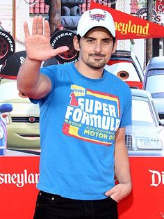 a man in a blue shirt and white hat waves at the camera