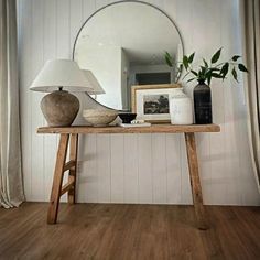 a wooden table topped with a lamp next to a mirror and vase on top of it