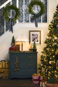 a christmas tree with two wreaths on it next to a dresser under the stairs