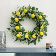 a wreath with lemons and greenery on a table next to a glass vase