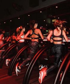 a group of women are running on treadmills in a gym with red lights