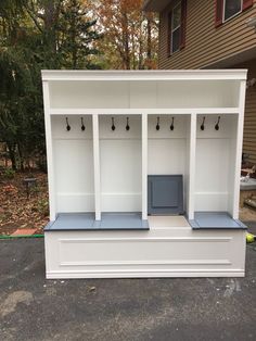 a white bench with two benches and some hooks on the back wall in front of a house