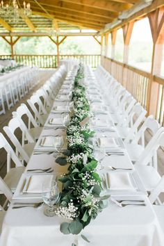 a long table with white chairs and greenery on the runneres is set up for an outdoor wedding