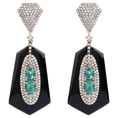 18.00 Carats Diamond, Emerald, and Black Onyx Drop Earrings in Art-Deco Style Feel unique with this scintillating and artistic set of earrings. The exquisite and artistic design with which this set of earrings is crafted, speaks a lot about it. This combination of black onyx, diamonds and emerald is what makes this pair of earrings a style statement. This art-deco style set of earrings is exceptional and a head-turner. The lower half of the earrings is crafted with an oval-shaped and one teardrop-shaped emerald placed opposite to each other. These pieces of emeralds are further surrounded by a cluster of diamonds in 3 consecutive halos making the emeralds stand out and look absolutely amplifying. These beautiful pieces of emerald are embellished over hexagon shaped tubes of black onyx exqu Luxury Black Art Deco Earrings, Art Deco Drop Earrings For Evening, Designer Drop Earrings For Evening, Art Deco Evening Gemstone Jewelry, Luxury Diamond Gemstone Earrings For Party, Luxury Gemstone Earrings For Party, Formal Black Diamond Earrings Fine Jewelry, Fine Jewelry Polished Finish Evening Earrings, Exquisite Evening Earrings With 17 Jewels