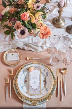 the table is set with gold and white plates, silverware, and floral centerpieces