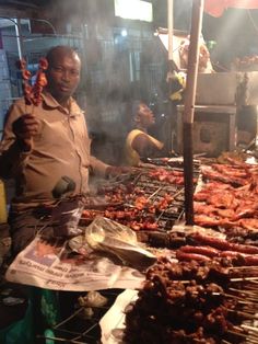 a man standing in front of a bbq filled with meats and sausages