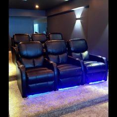 an empty home theater with black leather seats and blue lights on the wall behind it