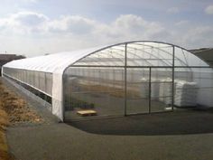 a large white greenhouse sitting on the side of a road next to a dirt field