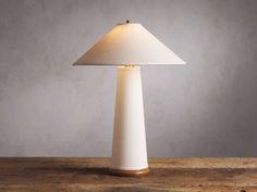 a white table lamp sitting on top of a wooden table next to a gray wall