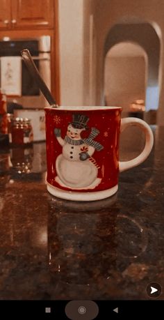 a red and white mug with a snowman on it sitting on a kitchen counter