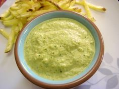 a bowl filled with green liquid next to some fries