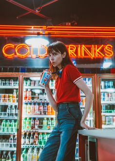 a woman leaning on a counter in front of a cold drinks store with neon signs