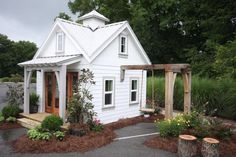 a small white house sitting on top of a lush green field next to a forest