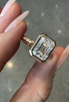 a woman's hand holding a ring with an emerald stone in the center and gold accents