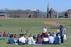 a group of people sitting on top of a lush green field next to a baseball field