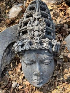 a head statue sitting on the ground next to leaves