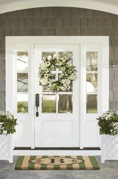 a white front door with two planters and a wreath on the side walk way